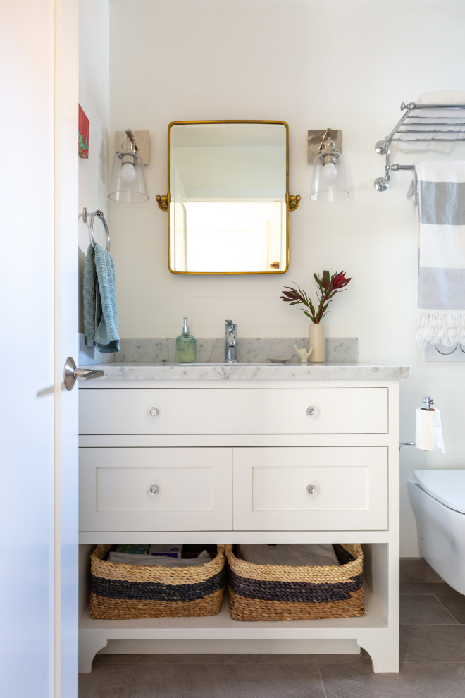 Inspiration for a mid-sized beach style kids bathroom in San Francisco with shaker cabinets, white cabinets, an alcove tub, a shower/bathtub combo, a wall-mount toilet, blue tile, subway tile, white walls, ceramic floors, an undermount sink, marble benchtops, grey floor, a shower curtain and grey benchtops.