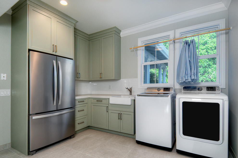 Large transitional l-shaped dedicated laundry room in San Francisco with a farmhouse sink, recessed-panel cabinets, green cabinets, quartz benchtops, grey walls, porcelain floors, a side-by-side washer and dryer, beige floor and white benchtop.