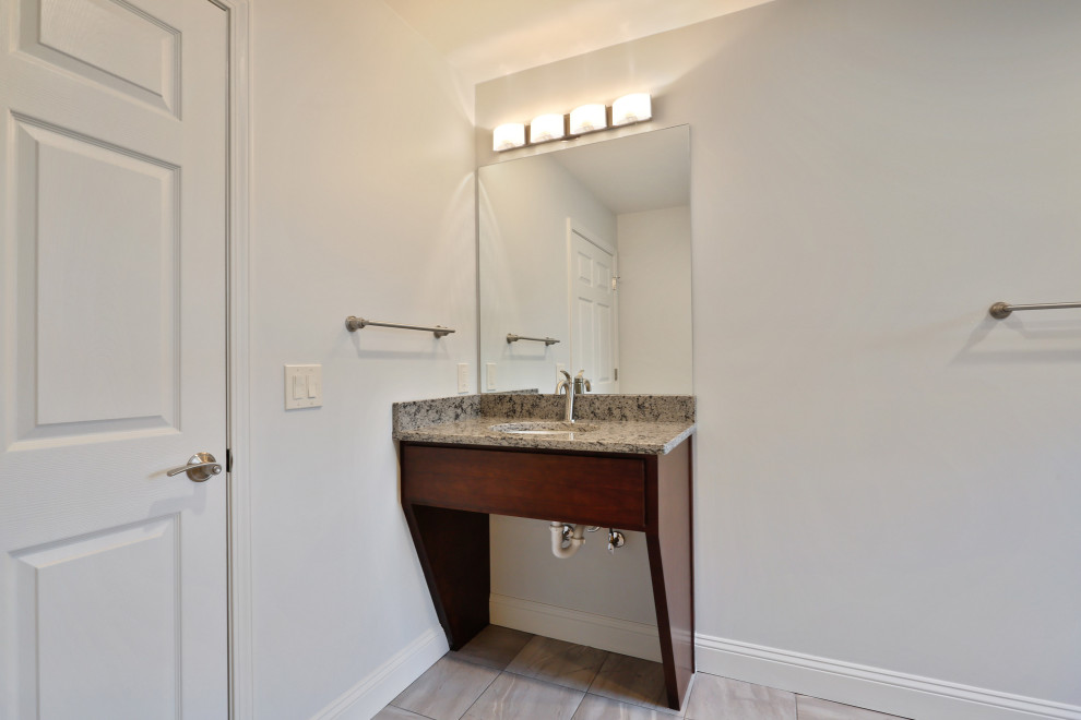 Photo of a large contemporary kids bathroom in Atlanta with shaker cabinets, brown cabinets, a shower/bathtub combo, a two-piece toilet, gray tile, ceramic tile, white walls, cement tiles, an integrated sink, granite benchtops, grey floor, a shower curtain, grey benchtops, a laundry, a single vanity and a freestanding vanity.