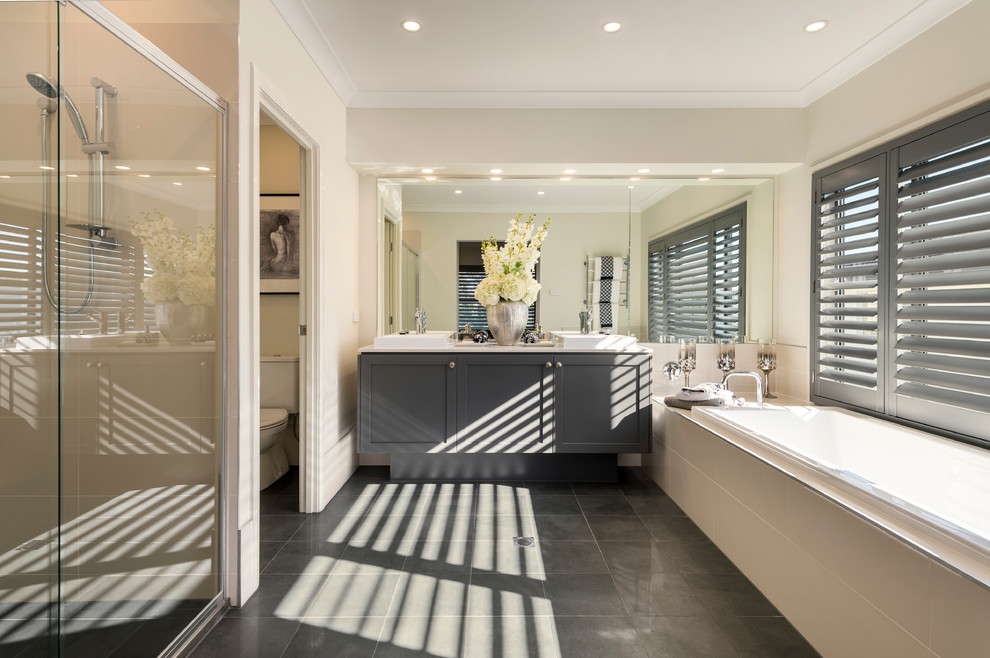 This is an example of a large contemporary master bathroom in Brisbane with shaker cabinets, grey cabinets, a drop-in tub, an alcove shower, a wall-mount toilet, beige tile, porcelain tile, beige walls, ceramic floors, a console sink and engineered quartz benchtops.