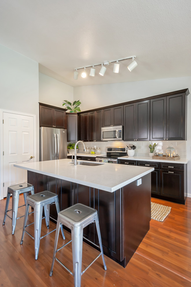 Inspiration for a mid-sized transitional l-shaped eat-in kitchen remodel in Phoenix with an undermount sink, raised-panel cabinets, black cabinets, quartz countertops, gray backsplash, porcelain backsplash, stainless steel appliances, an island and white countertops