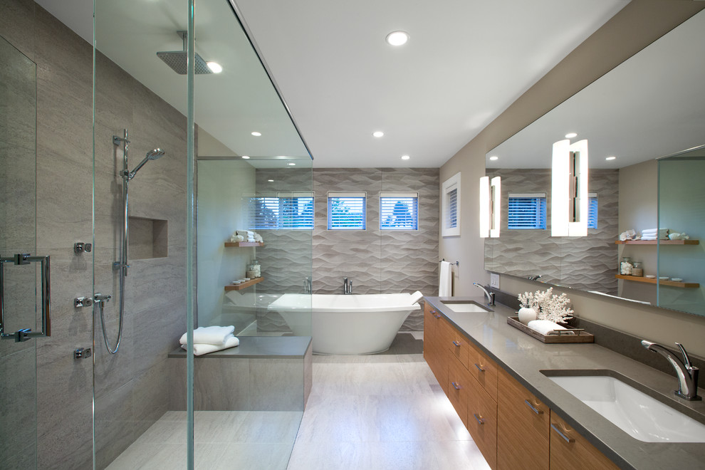 Photo of a large contemporary master bathroom in Vancouver with flat-panel cabinets, medium wood cabinets, a freestanding tub, a curbless shower, gray tile, beige walls, an undermount sink, porcelain tile, porcelain floors, engineered quartz benchtops, beige floor, a hinged shower door and grey benchtops.