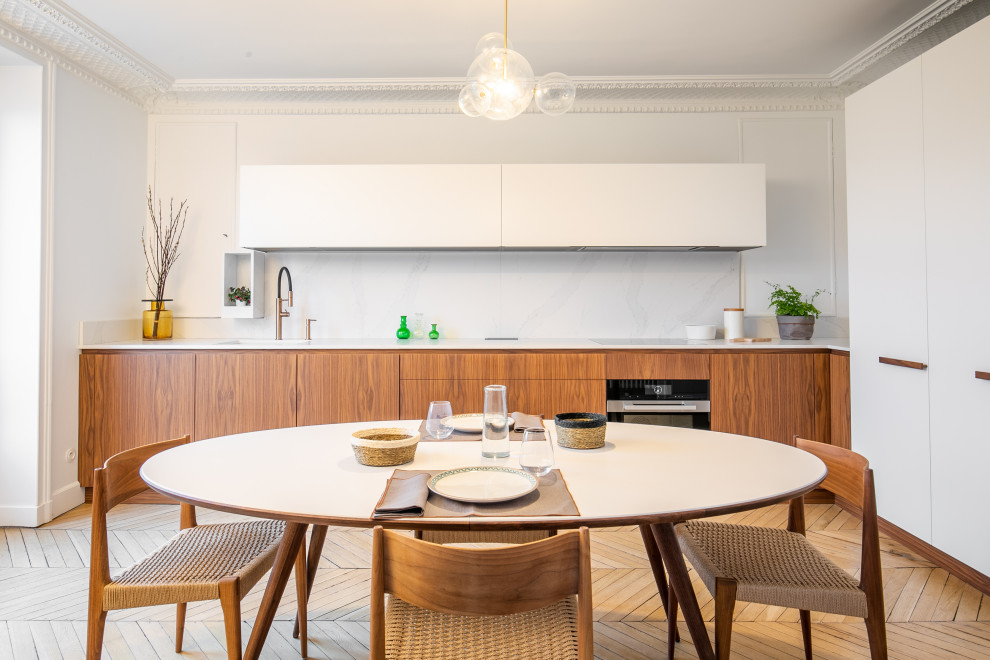 Large contemporary l-shaped open plan kitchen in Paris with an undermount sink, light wood cabinets, quartzite benchtops, white splashback, marble splashback, black appliances, white benchtop, flat-panel cabinets, medium hardwood floors and brown floor.