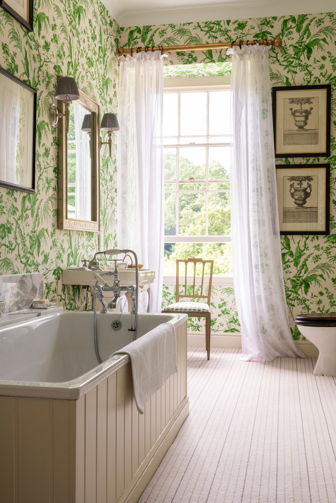 Photo of a large traditional bathroom with a drop-in tub, multi-coloured walls, a pedestal sink, beige floor and wallpaper.