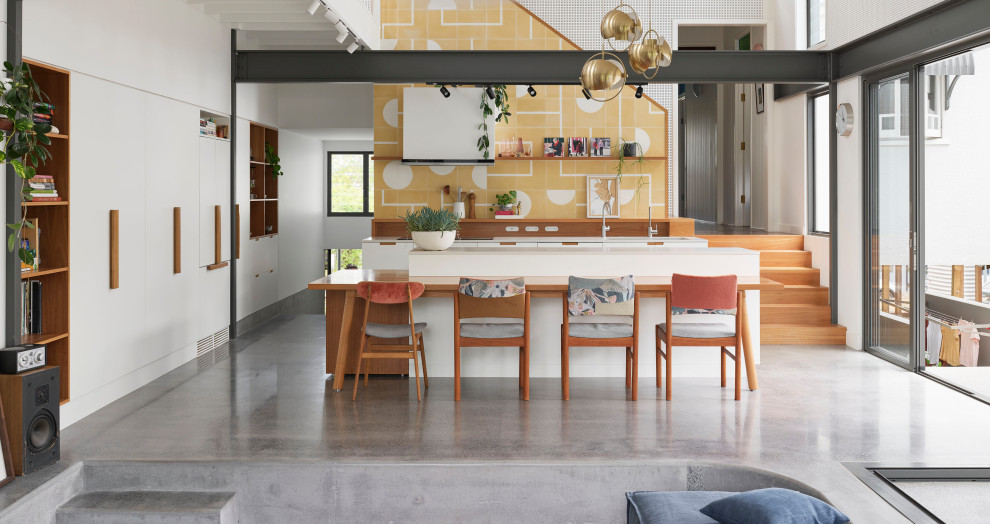Contemporary kitchen in Brisbane with quartz benchtops, yellow splashback, cement tile splashback, white appliances, concrete floors, grey floor, white benchtop and exposed beam.
