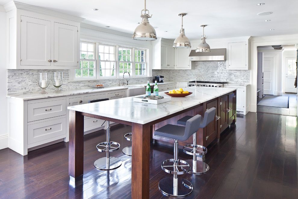 Example of a large transitional l-shaped dark wood floor and brown floor eat-in kitchen design in New York with white cabinets, marble countertops, white backsplash, an island, a farmhouse sink, shaker cabinets, matchstick tile backsplash and stainless steel appliances