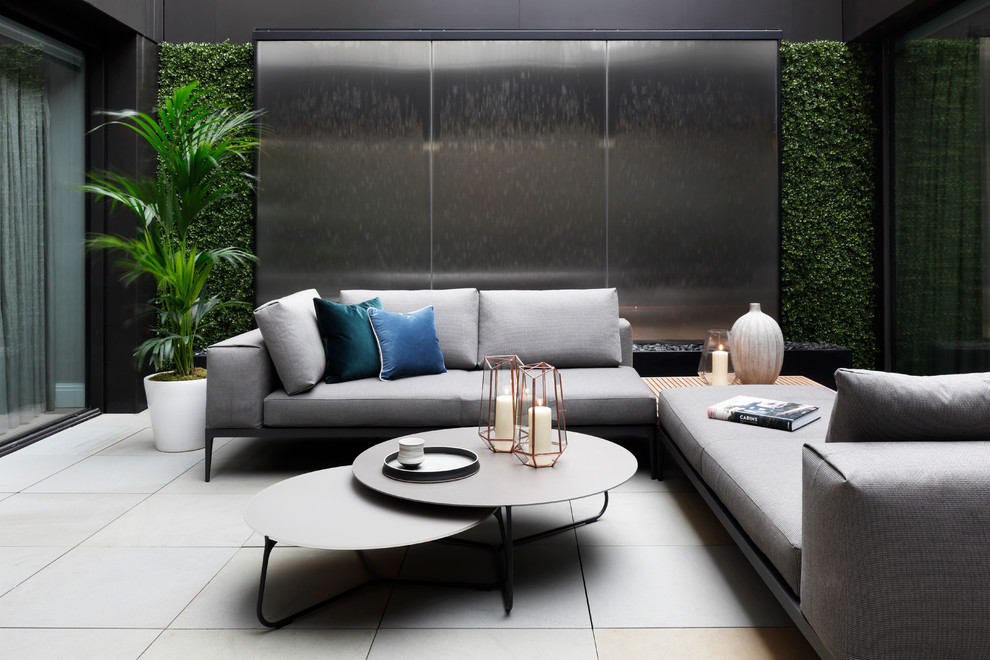 This is an example of a mid-sized contemporary courtyard patio in London with a water feature, tile and no cover.