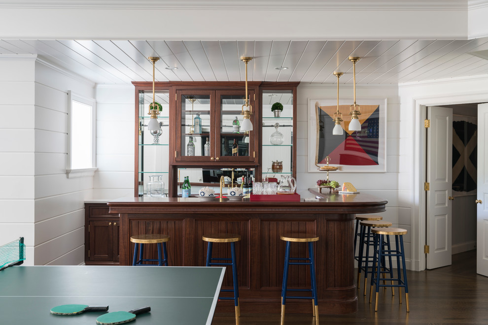 This is an example of an expansive traditional l-shaped wet bar in New York with dark hardwood floors, brown floor, an undermount sink, glass-front cabinets, medium wood cabinets, wood benchtops, mirror splashback and brown benchtop.