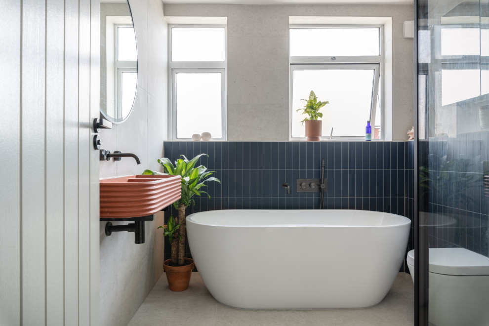 This is an example of a mid-sized contemporary kids bathroom in London with a freestanding tub, an open shower, a one-piece toilet, gray tile, porcelain tile, grey walls, porcelain floors, a wall-mount sink, concrete benchtops, grey floor, a hinged shower door, orange benchtops and a single vanity.