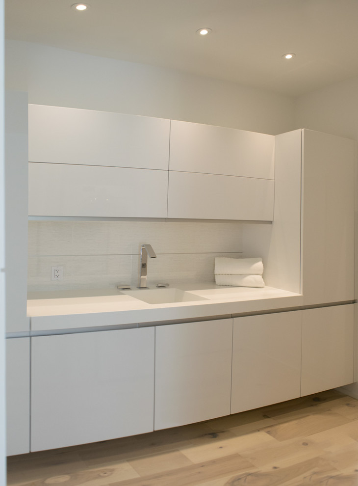 Design ideas for a mid-sized modern single-wall dedicated laundry room in Miami with an integrated sink, flat-panel cabinets, white cabinets, quartz benchtops, white walls, light hardwood floors, a concealed washer and dryer and beige floor.