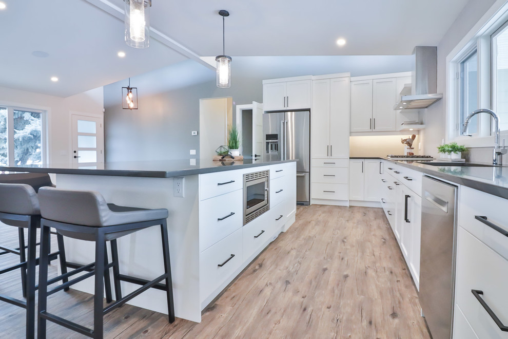 Example of a large transitional l-shaped vinyl floor and brown floor open concept kitchen design with an undermount sink, flat-panel cabinets, white cabinets, quartz countertops, gray backsplash, porcelain backsplash, stainless steel appliances and an island