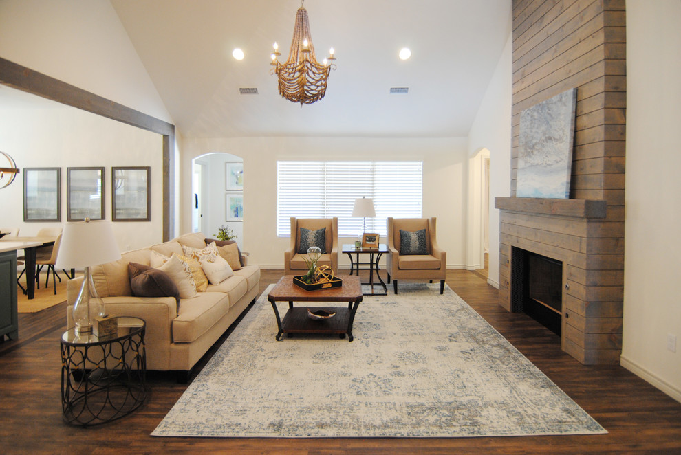 This is an example of a large country open concept living room with white walls, vinyl floors, a standard fireplace, a wood fireplace surround, a wall-mounted tv and brown floor.