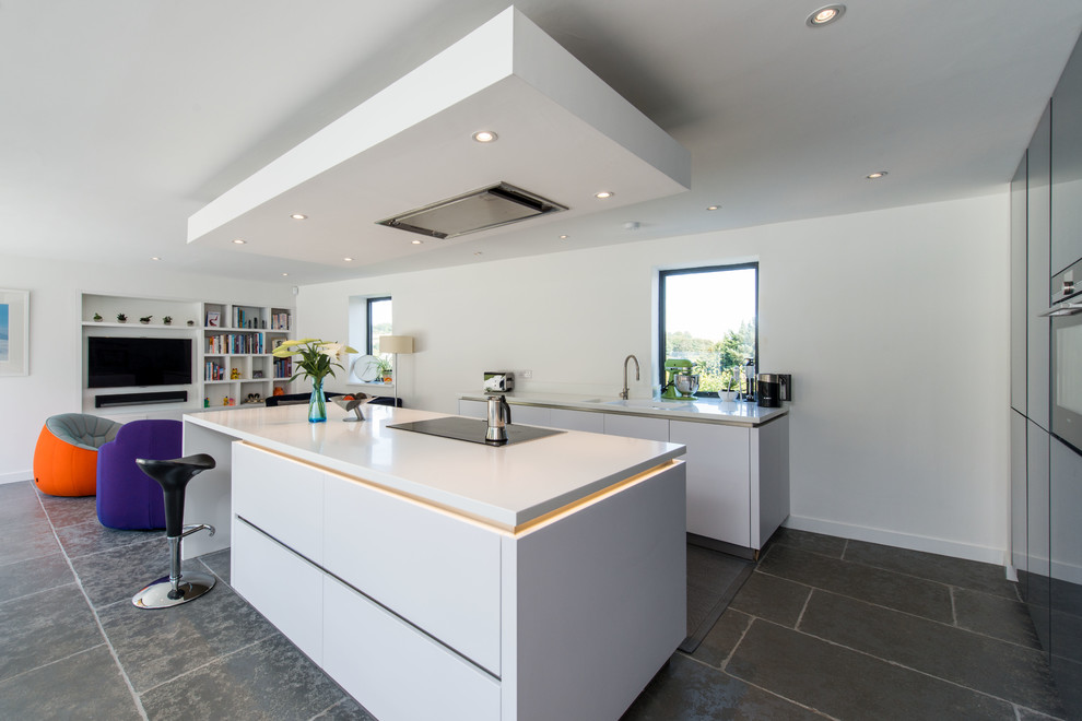 This is an example of a contemporary kitchen in Other with a drop-in sink, flat-panel cabinets, solid surface benchtops, black appliances, limestone floors, with island and grey floor.