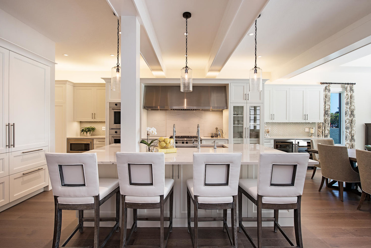 Photo of a transitional kitchen in Miami with shaker cabinets, white cabinets, white splashback, white appliances, medium hardwood floors and brown floor.