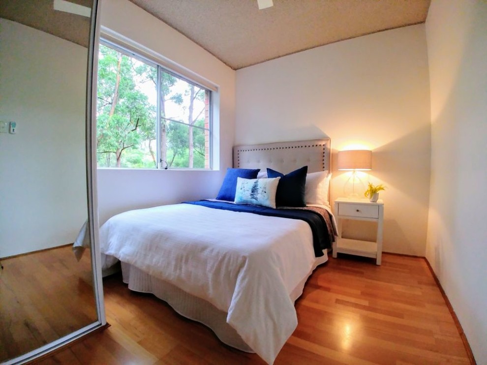 Photo of a mid-sized contemporary guest bedroom in Sydney with white walls, laminate floors and multi-coloured floor.