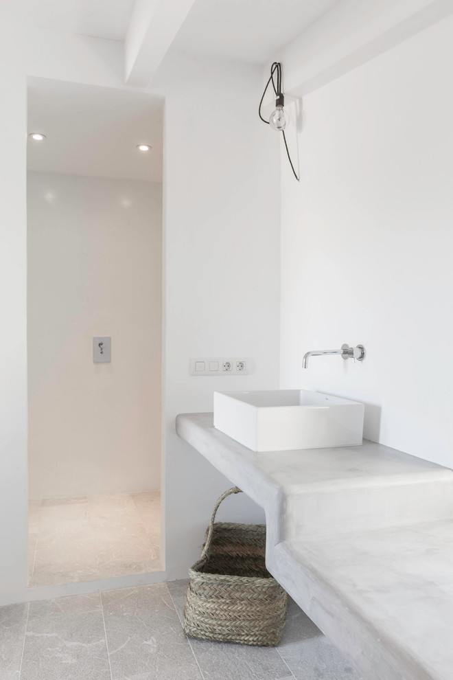 This is an example of a mediterranean bathroom in London with an open shower, white walls, limestone floors, a vessel sink, concrete benchtops and an open shower.