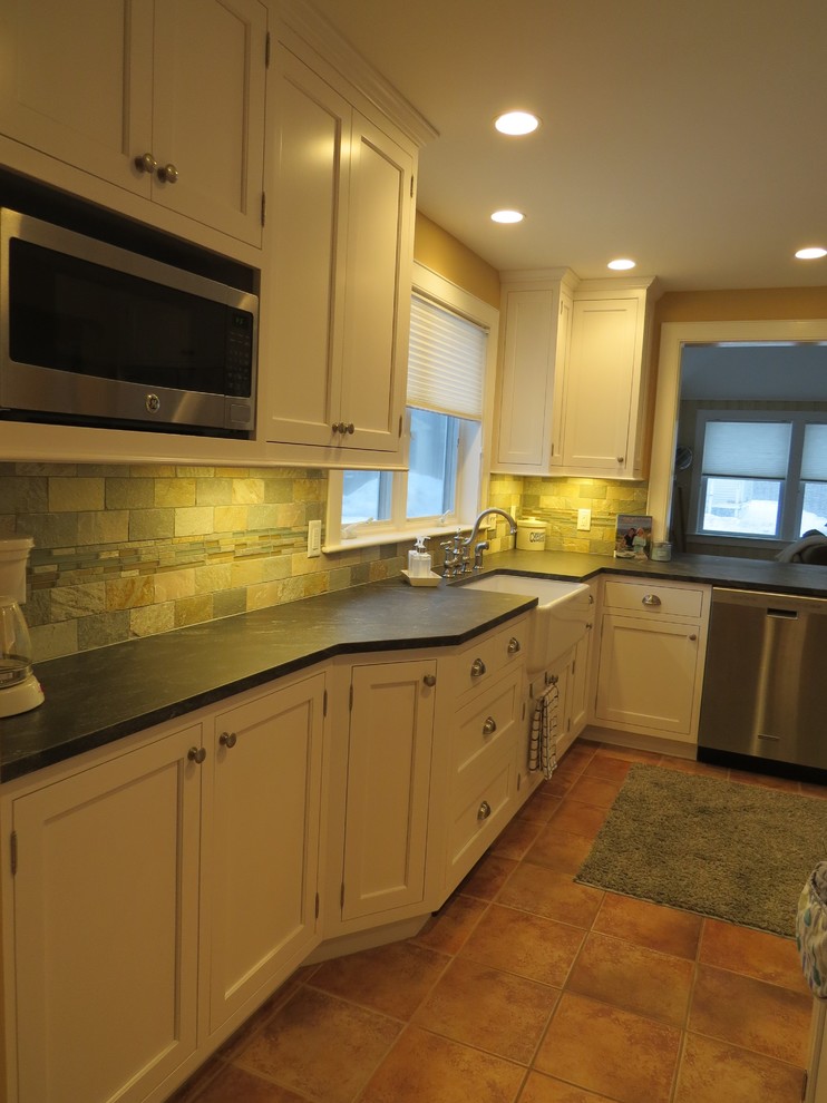 This is an example of a mid-sized beach style l-shaped eat-in kitchen in Portland Maine with a farmhouse sink, beaded inset cabinets, white cabinets, granite benchtops, multi-coloured splashback, stone tile splashback, stainless steel appliances, ceramic floors and with island.