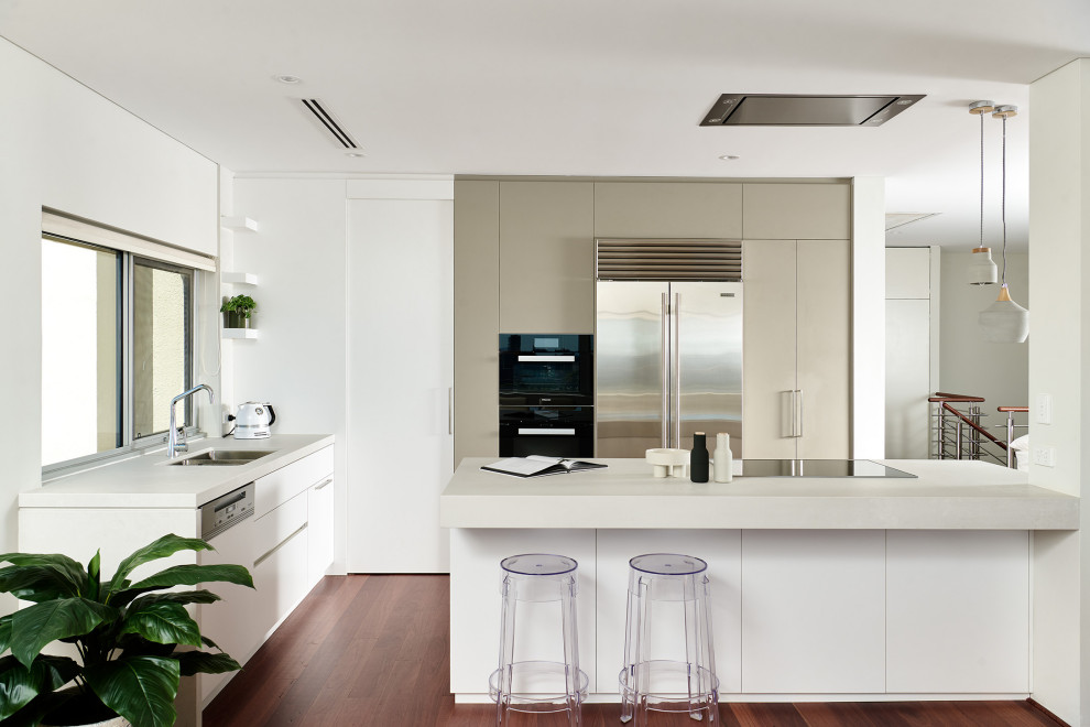 Medium sized modern l-shaped open plan kitchen in Perth with a submerged sink, flat-panel cabinets, white cabinets, engineered stone countertops, white splashback, ceramic splashback, black appliances, dark hardwood flooring, an island, brown floors, white worktops and all types of ceiling.