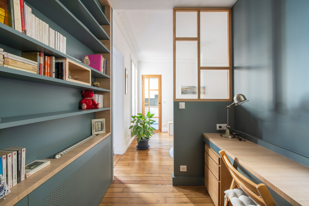 This is an example of a small scandinavian home office in Paris with a library, blue walls, medium hardwood floors, no fireplace, a built-in desk and beige floor.
