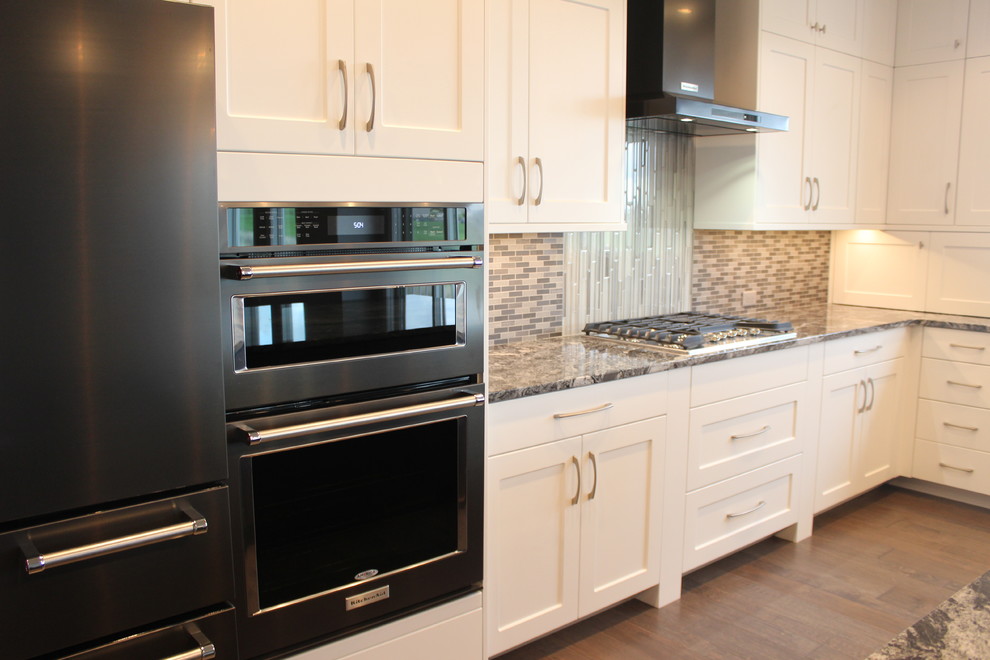 Inspiration for a large transitional l-shaped medium tone wood floor and brown floor kitchen remodel with an undermount sink, shaker cabinets, white cabinets, granite countertops, multicolored backsplash, mosaic tile backsplash, black appliances and an island