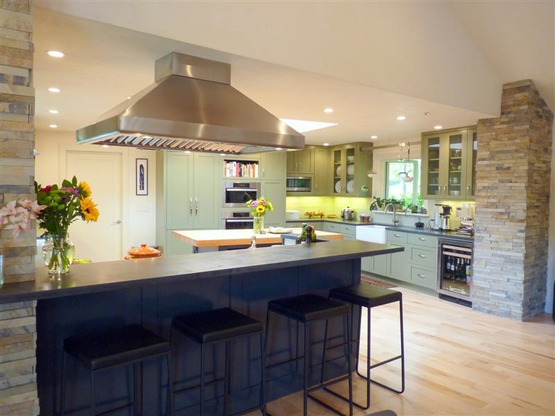 This is an example of a large transitional open plan kitchen in San Francisco with a farmhouse sink, shaker cabinets, green cabinets, white splashback, glass tile splashback, stainless steel appliances, light hardwood floors and with island.