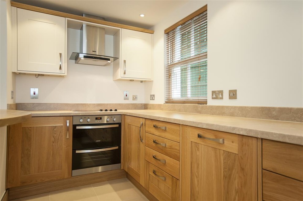 Photo of a small contemporary galley eat-in kitchen in Hertfordshire with a drop-in sink, raised-panel cabinets, medium wood cabinets, marble benchtops, beige splashback, slate splashback, stainless steel appliances, ceramic floors, a peninsula and beige floor.