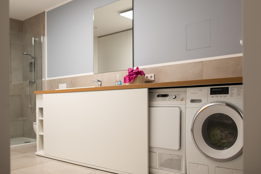 Photo of a large contemporary u-shaped utility room in Other with a drop-in sink, flat-panel cabinets, white cabinets, grey walls and an integrated washer and dryer.