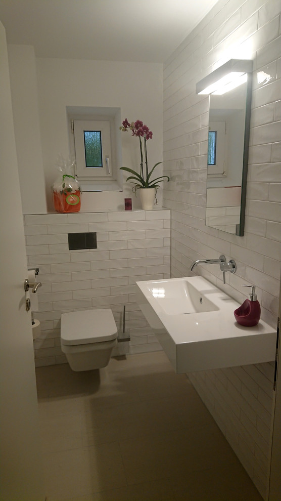 Inspiration for a small contemporary powder room in Berlin with a two-piece toilet, white tile, subway tile, white walls, a wall-mount sink, beige floor, flat-panel cabinets, blue cabinets, ceramic floors, stainless steel benchtops and white benchtops.