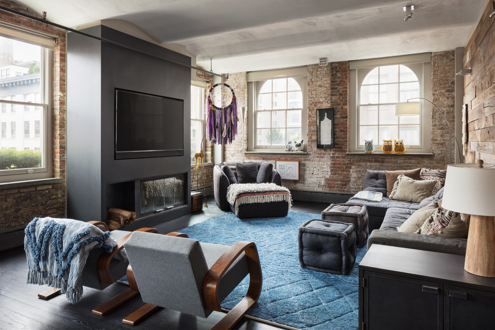 Photo of an industrial living room in New York with dark hardwood floors, a standard fireplace, a wall-mounted tv and brown floor.