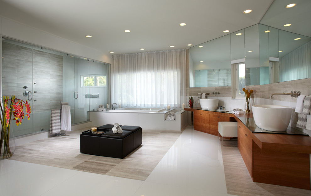 This is an example of a large contemporary master bathroom in Miami with flat-panel cabinets, light wood cabinets, a drop-in tub, a double shower, a one-piece toilet, beige tile, marble, white walls, marble floors, a vessel sink, glass benchtops, multi-coloured floor and a hinged shower door.