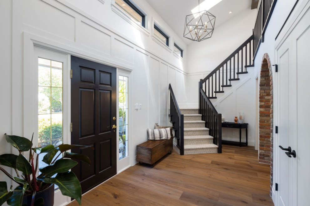 Example of a mid-sized transitional medium tone wood floor, brown floor and wall paneling foyer design in Vancouver with white walls and a black front door