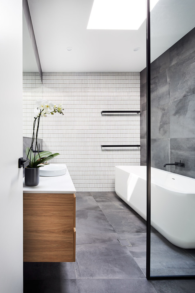 Photo of a contemporary master bathroom in Sydney with medium wood cabinets, a freestanding tub, a curbless shower, gray tile, a vessel sink, grey floor and white benchtops.