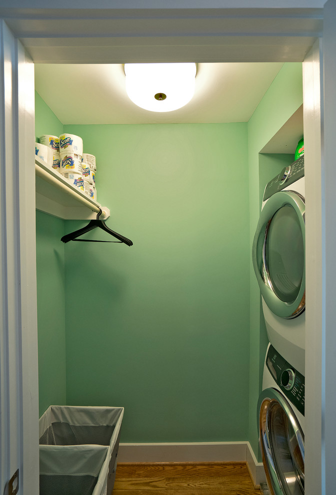 Design ideas for a small transitional laundry cupboard in DC Metro with green walls, medium hardwood floors, a stacked washer and dryer and brown floor.