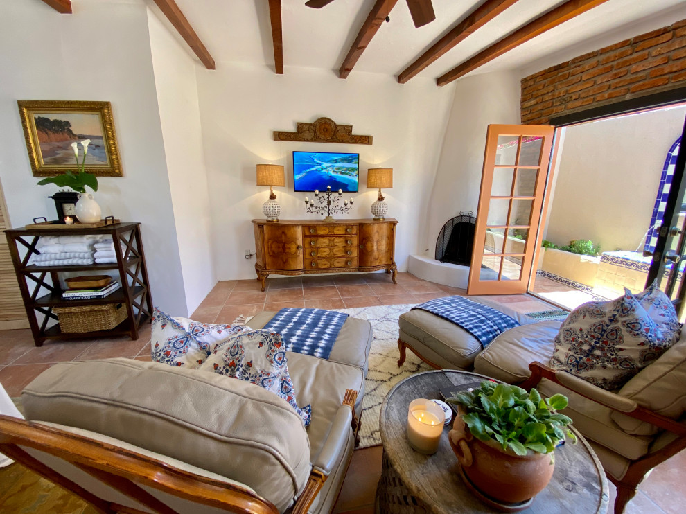 Design ideas for a mid-sized mediterranean open concept living room in Other with white walls, terra-cotta floors, a corner fireplace, a plaster fireplace surround, a wall-mounted tv, orange floor, exposed beam and brick walls.