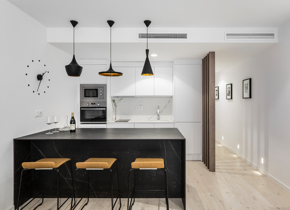 Mid-sized contemporary kitchen in Valencia with an undermount sink, flat-panel cabinets, white splashback, marble splashback, stainless steel appliances, light hardwood floors, a peninsula and beige floor.