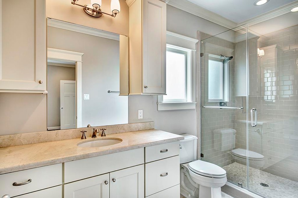 Mid-sized transitional 3/4 bathroom in Houston with shaker cabinets, white cabinets, an alcove shower, a two-piece toilet, limestone, grey walls, pebble tile floors, an undermount sink, grey floor and a hinged shower door.