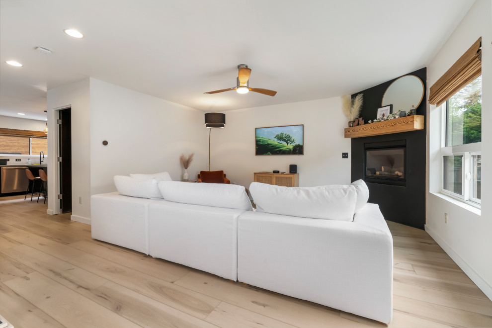 This is an example of a large midcentury formal open concept living room in Seattle with white walls, a standard fireplace, a plaster fireplace surround, a wall-mounted tv, beige floor and vinyl floors.