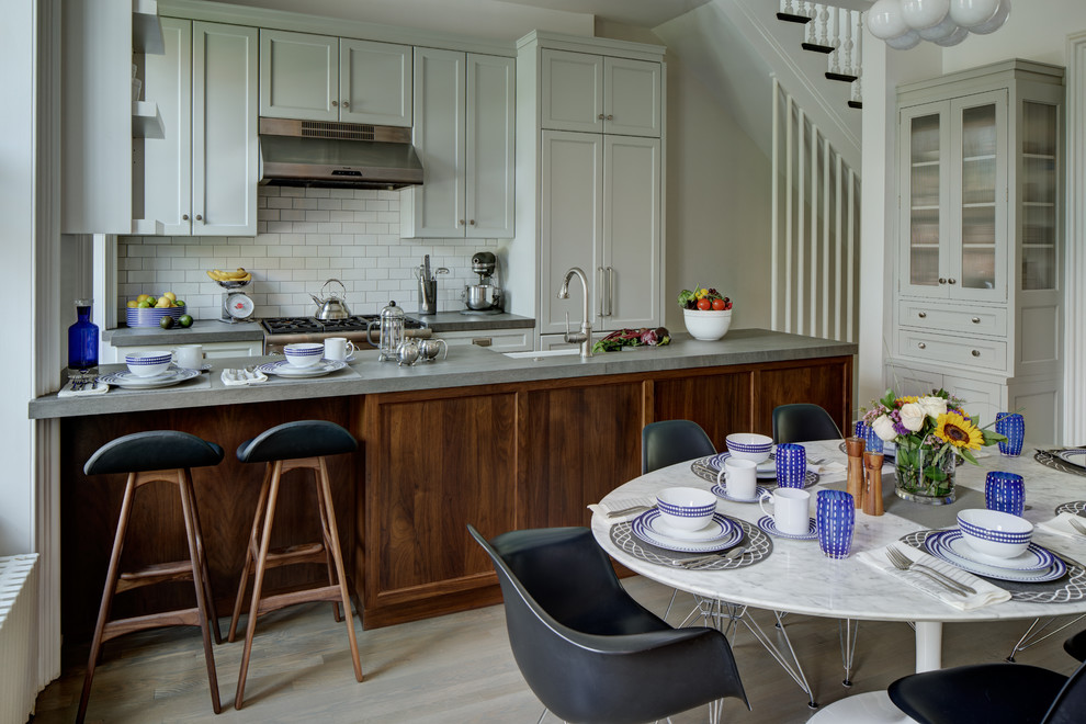Transitional galley light wood floor eat-in kitchen photo with a farmhouse sink, shaker cabinets, white cabinets, white backsplash, subway tile backsplash, paneled appliances and a peninsula