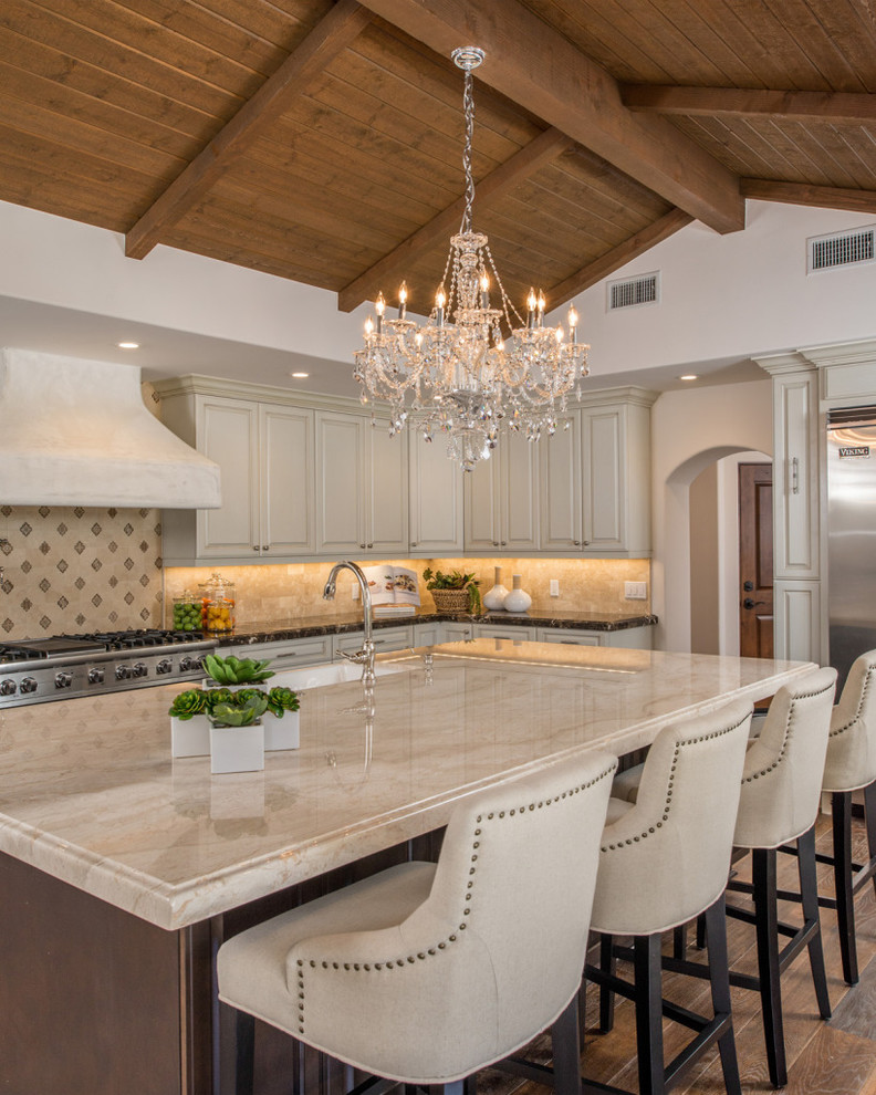 This is an example of a large mediterranean u-shaped eat-in kitchen in San Diego with a farmhouse sink, raised-panel cabinets, white cabinets, marble benchtops, beige splashback, ceramic splashback, stainless steel appliances, dark hardwood floors and with island.