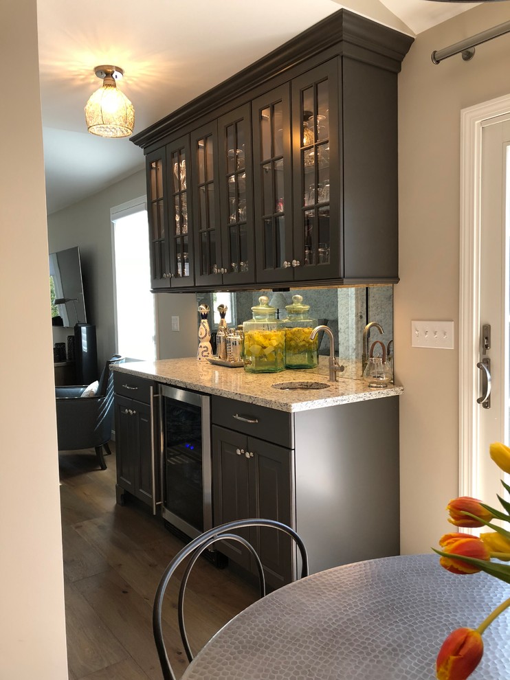 Inspiration for a large transitional l-shaped open plan kitchen in Boston with an undermount sink, shaker cabinets, white cabinets, granite benchtops, white splashback, subway tile splashback, stainless steel appliances, medium hardwood floors, with island, brown floor and black benchtop.