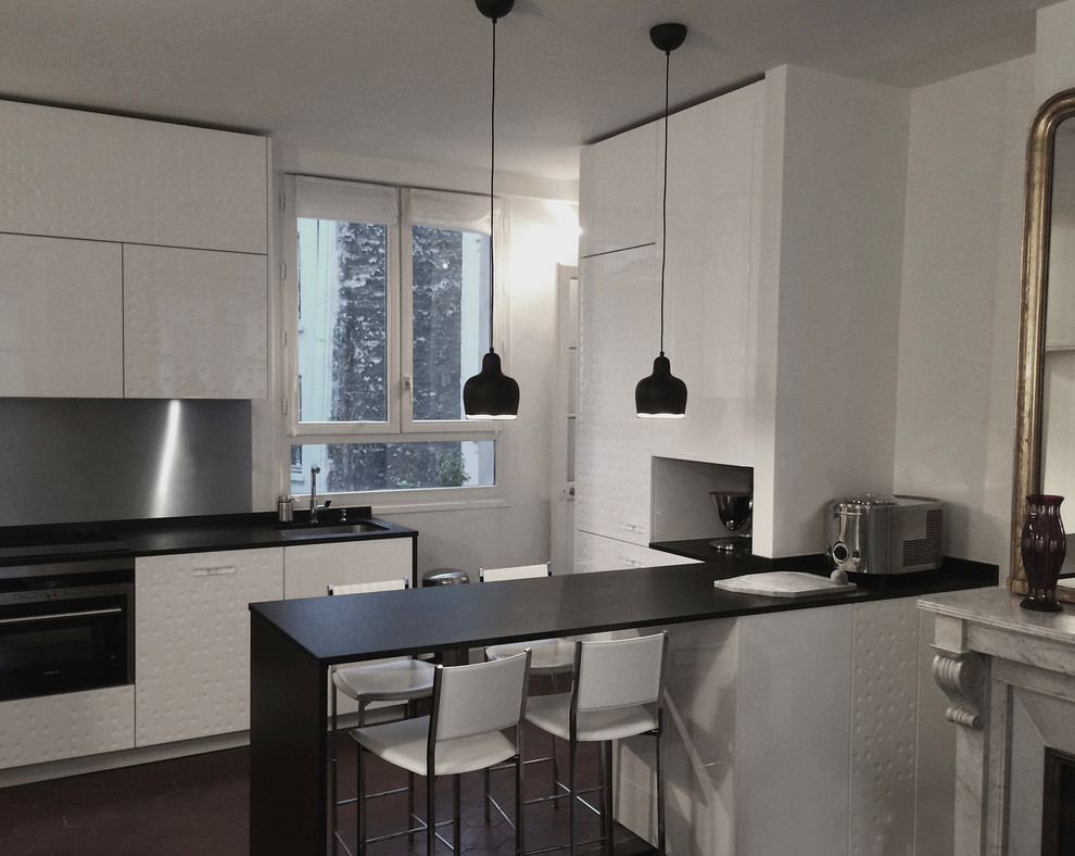 This is an example of a modern single-wall eat-in kitchen in London with an undermount sink, flat-panel cabinets, white cabinets, granite benchtops, metallic splashback and stainless steel appliances.