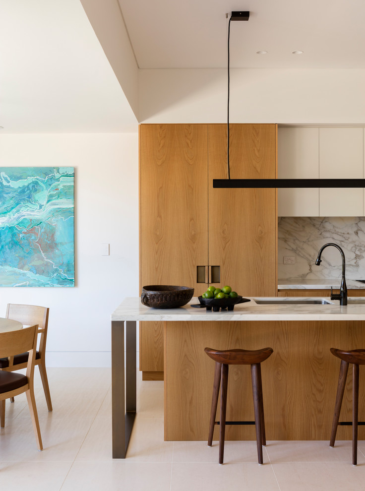 Contemporary eat-in kitchen in Sydney with an undermount sink, flat-panel cabinets, light wood cabinets, white splashback, with island, beige floor and white benchtop.
