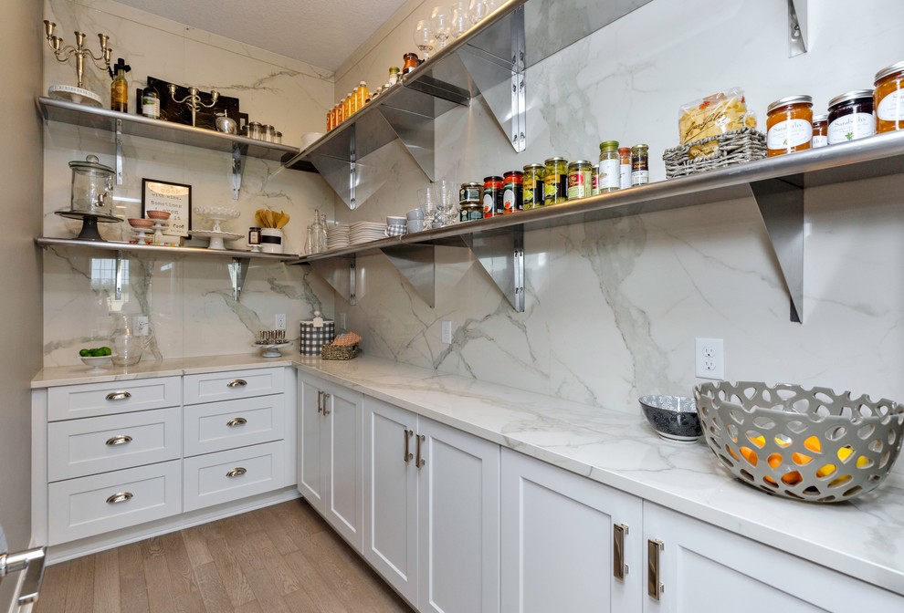 Large transitional l-shaped porcelain tile eat-in kitchen photo with a farmhouse sink, shaker cabinets, white cabinets, marble countertops, stainless steel appliances and an island