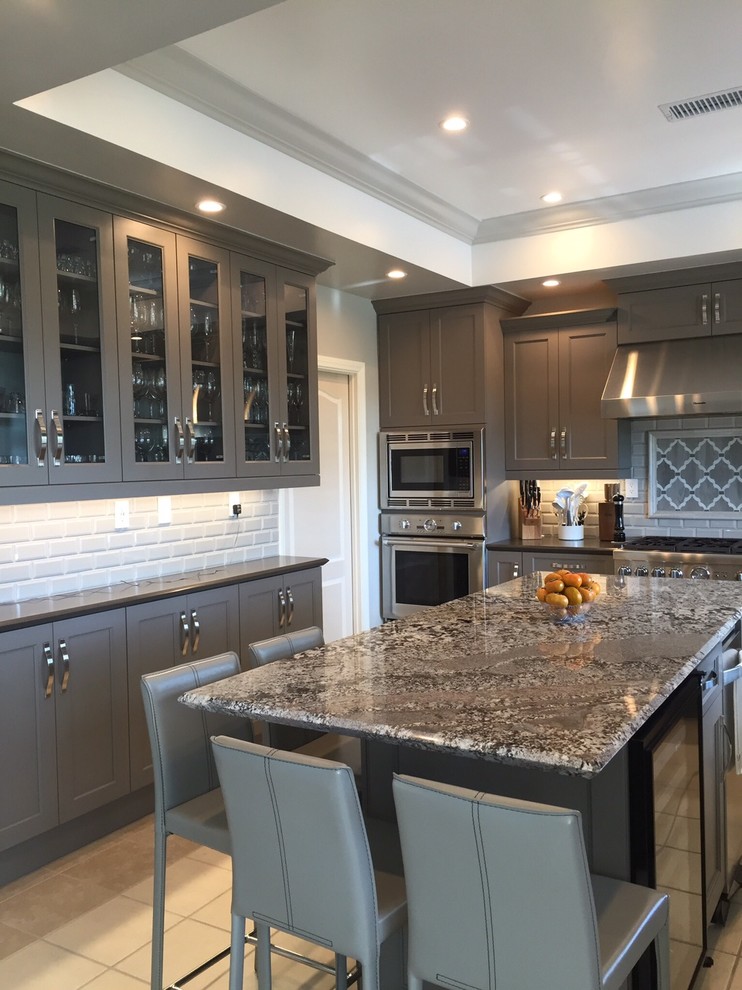 Kitchen pantry - large transitional u-shaped porcelain tile kitchen pantry idea in Los Angeles with a farmhouse sink, shaker cabinets, gray cabinets, granite countertops, beige backsplash, ceramic backsplash, stainless steel appliances and an island