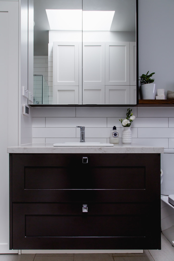 Photo of a mid-sized contemporary master bathroom in Melbourne with shaker cabinets, brown cabinets, a freestanding tub, a wall-mount toilet, white tile, porcelain tile, grey walls, porcelain floors, a drop-in sink, engineered quartz benchtops, white floor, white benchtops and a hinged shower door.