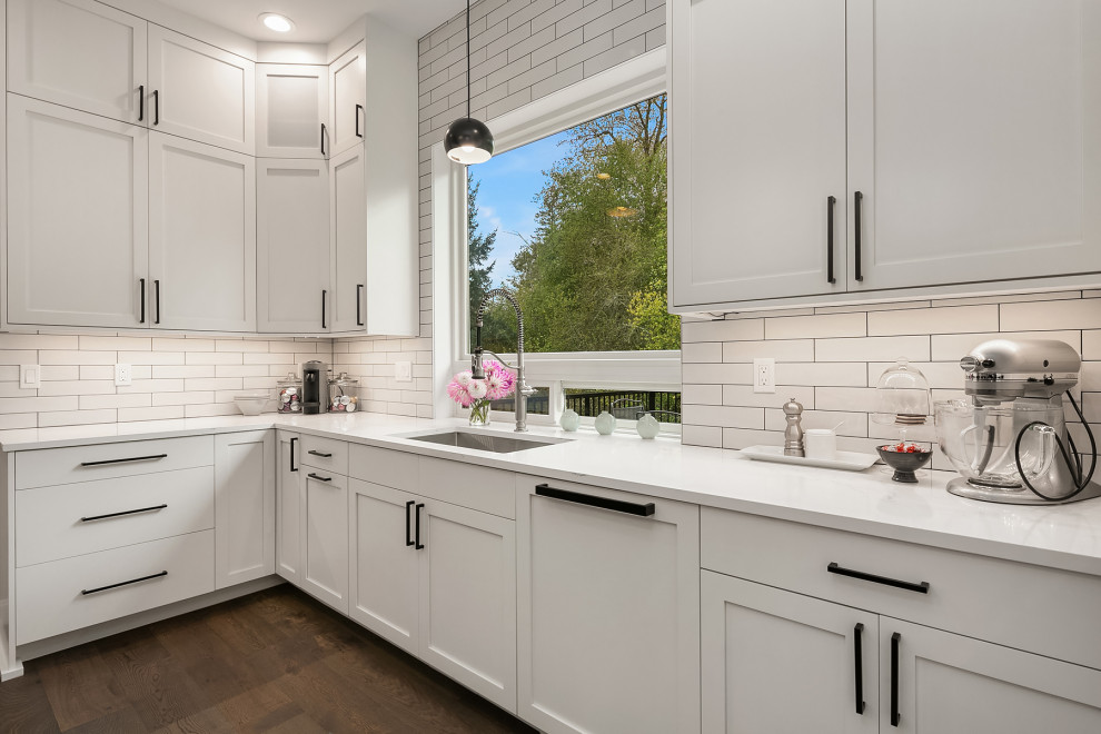 Example of a large transitional medium tone wood floor and gray floor kitchen design in Seattle with an undermount sink, shaker cabinets, white cabinets, quartz countertops, white backsplash, subway tile backsplash, stainless steel appliances, an island and white countertops