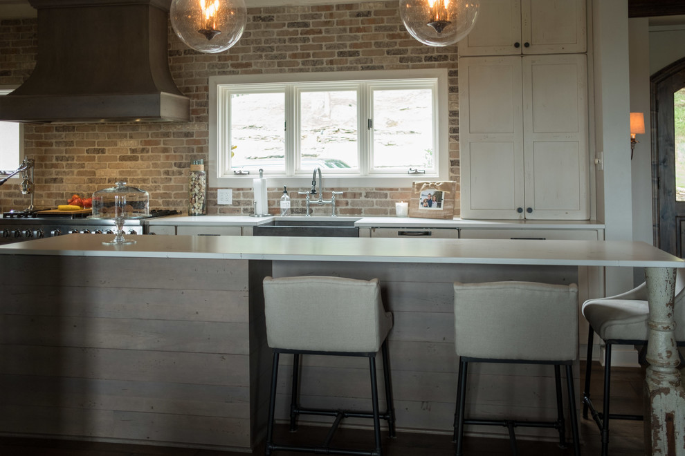 Large transitional galley dark wood floor and brown floor open concept kitchen photo with a farmhouse sink, shaker cabinets, quartz countertops, brown backsplash, brick backsplash, stainless steel appliances and an island