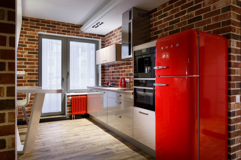 Industrial single-wall eat-in kitchen in Saint Petersburg with flat-panel cabinets, white cabinets, beige benchtop, brick splashback, coloured appliances and light hardwood floors.