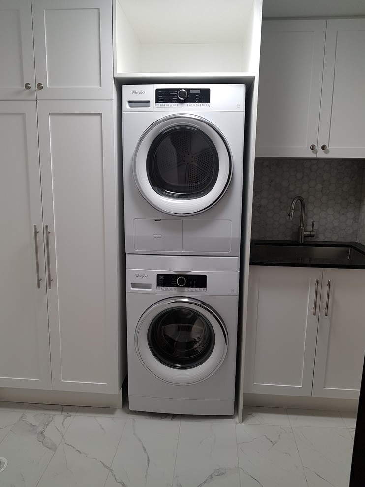 Large transitional single-wall dedicated laundry room in Toronto with an undermount sink, shaker cabinets, white cabinets, quartz benchtops, marble floors, a stacked washer and dryer and white floor.