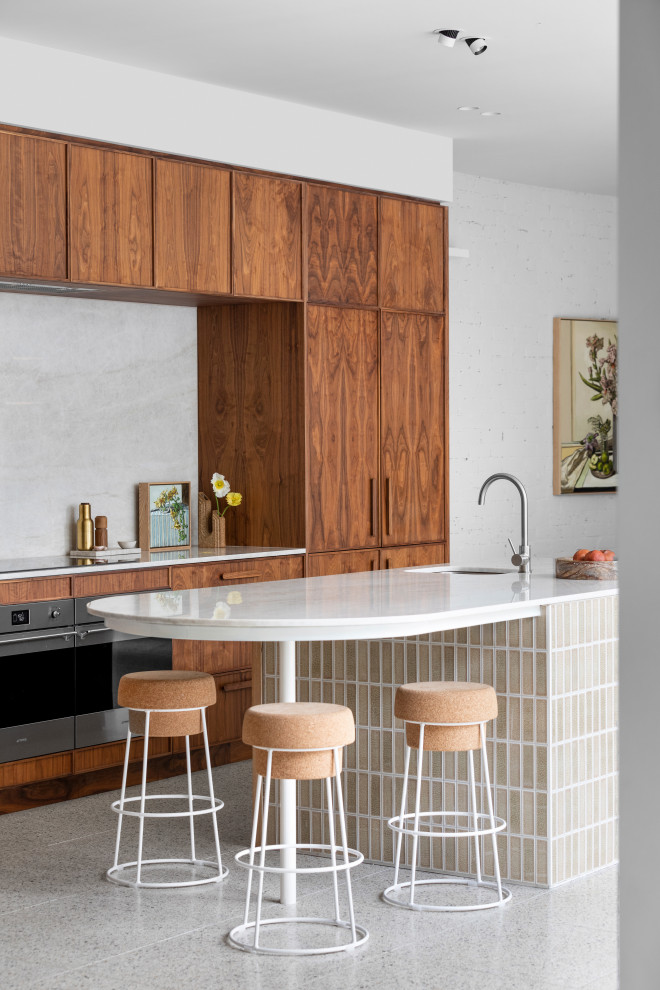 Large contemporary galley kitchen pantry in Melbourne with dark wood cabinets, stainless steel appliances, terrazzo floors, with island, an undermount sink, shaker cabinets, grey splashback, multi-coloured floor and white benchtop.